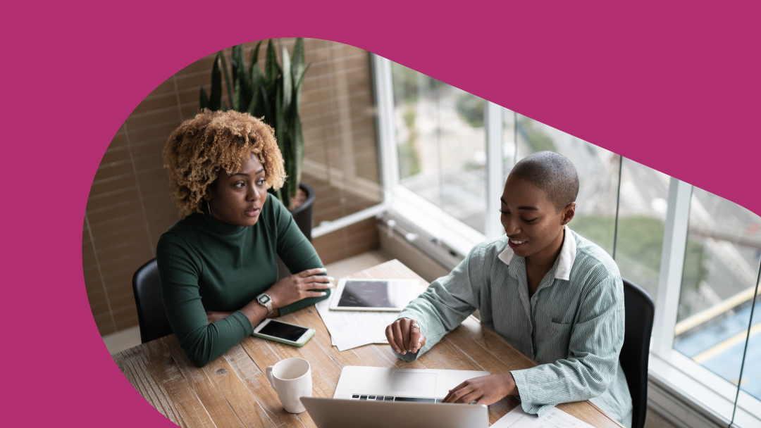 Two black women sitting at a table with a tablet and a laptop